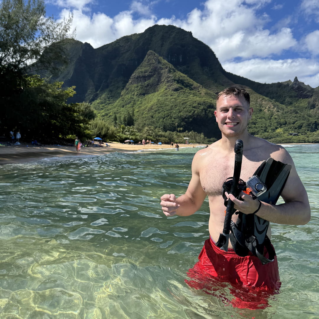Man holding snorkeling gear in clear water with mountains in the background